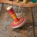 Mader wooden my first spinning top toy with starter in red placed on a wooden surface in the Babipur playroom.