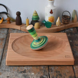 Mader wooden my first spinning top toy with starter in green placed on a large cherry wood spinning plate in the Babipur playroom.