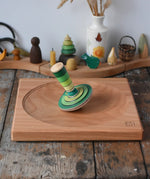 Mader wooden my first spinning top toy with starter in green placed on a large cherry wood spinning plate in the Babipur playroom.