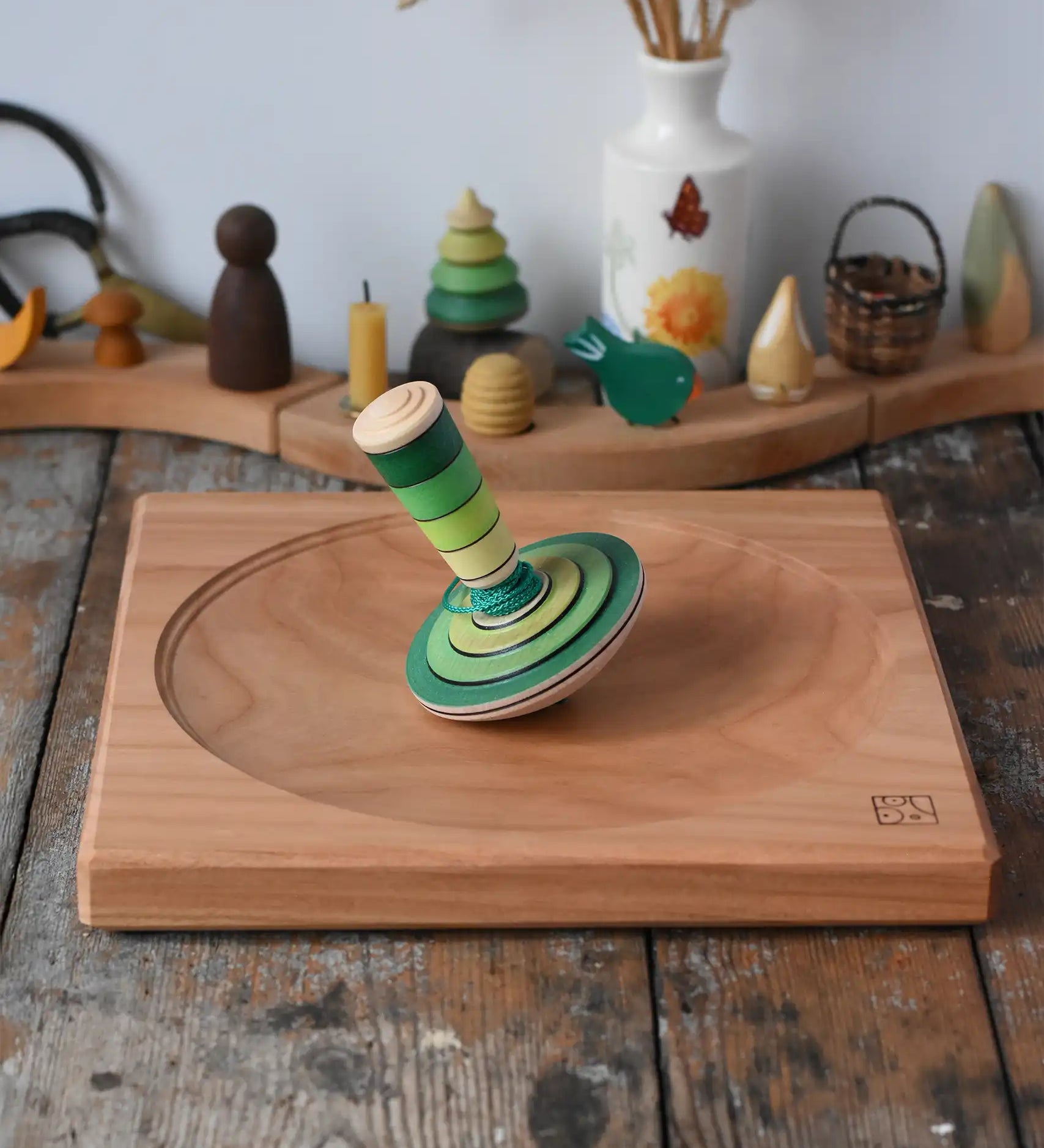 Mader wooden my first spinning top toy with starter in green placed on a large cherry wood spinning plate in the Babipur playroom.