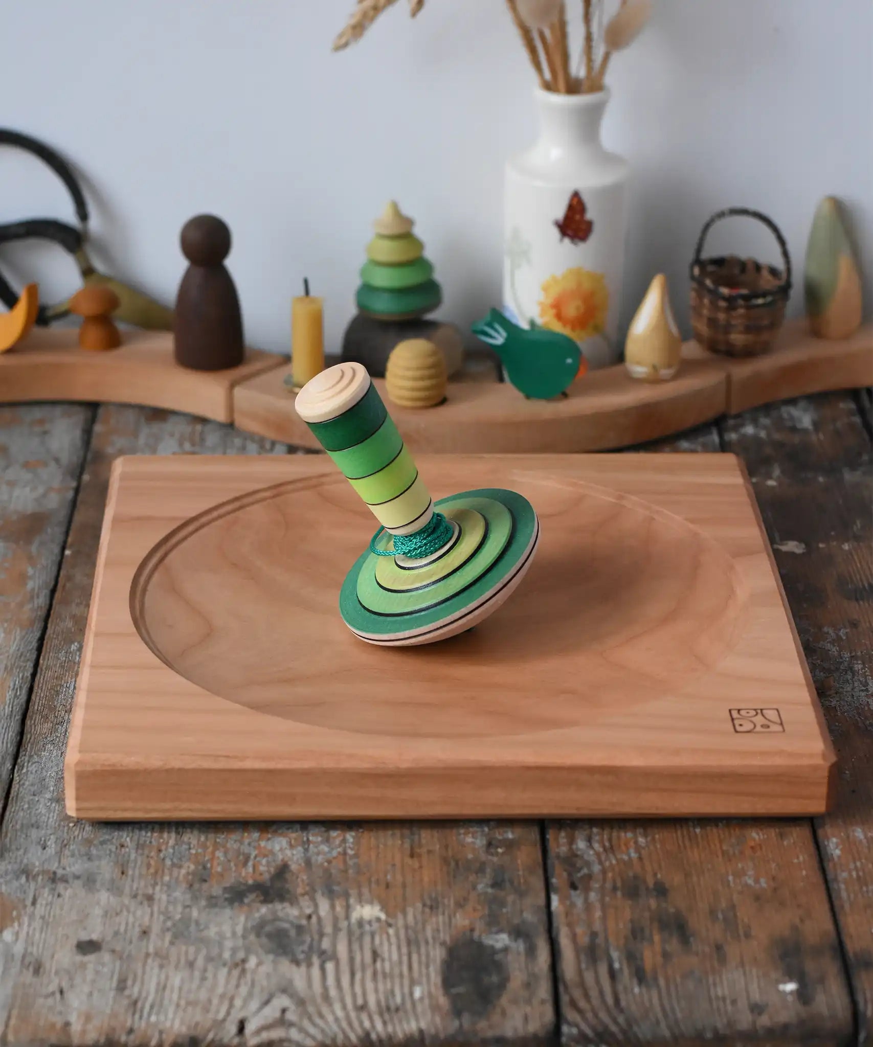 Mader wooden my first spinning top toy with starter in green placed on a large cherry wood spinning plate in the Babipur playroom.