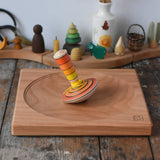 Mader wooden my first spinning top toy with starter in orange placed on a large cherry woodn spinning plate in the Babipur playroom.