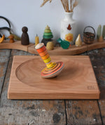 Mader wooden my first spinning top toy with starter in orange placed on a large cherry woodn spinning plate in the Babipur playroom.