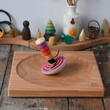 Mader my first spinning top toy with starter in pink placed on a large cherry wood spinning plate in the Babipur playroom. 
