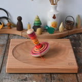 Mader wooden my first spinning top toy with starter in red placed on a large cherry wood spinning plate in the Babipur playroom.