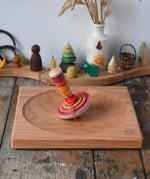 Mader wooden my first spinning top toy with starter in red placed on a large cherry wood spinning plate in the Babipur playroom.
