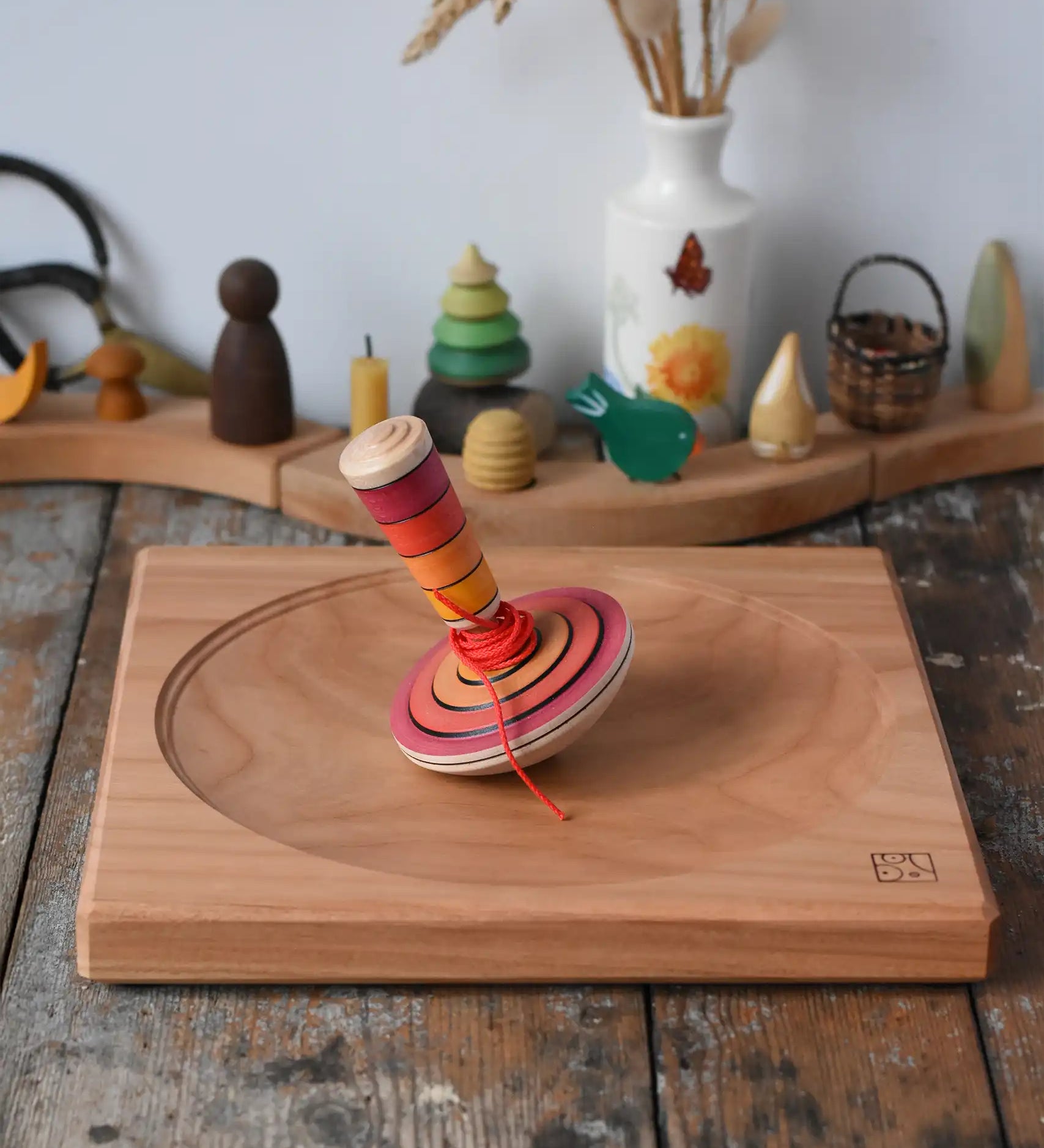 Mader wooden my first spinning top toy with starter in red placed on a large cherry wood spinning plate in the Babipur playroom.