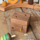 Mader Kreiselmanufaktur forest music box placed on a wooden desk in the Babipur playroom. A wooden wind up musical box with two slots for the green tree shaped spinners on the top. The two trees have been placed besides the box.