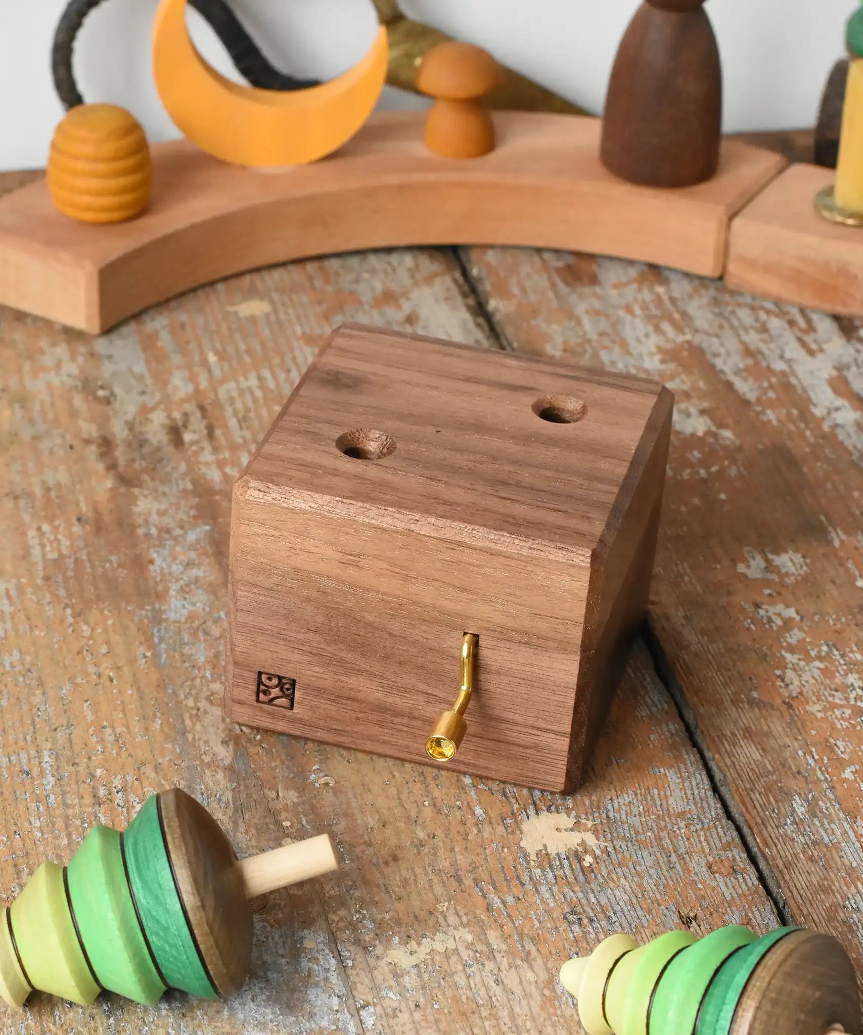 Mader Kreiselmanufaktur forest music box placed on a wooden desk in the Babipur playroom. A wooden wind up musical box with two slots for the green tree shaped spinners on the top. The two trees have been placed besides the box.
