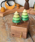 Mader Kreiselmanufaktur forest music box placed on a wooden desk in the Babipur playroom. A wooden wind up musical box with two slots for the green tree shaped spinners on the top.