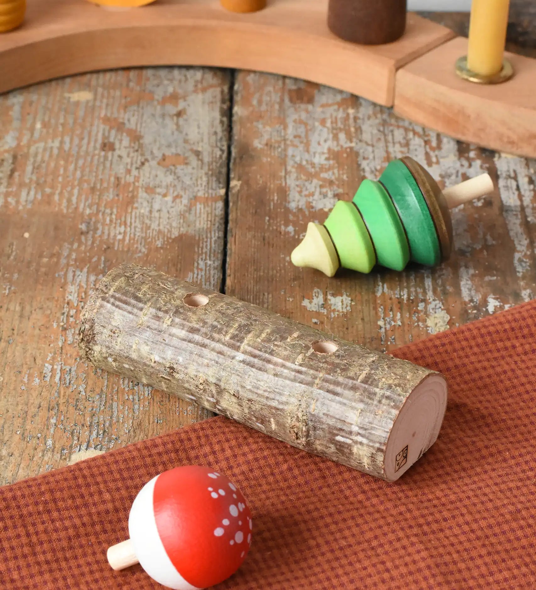 Mader Kreiselmanufaktur forest spinning top set. Green tree spinner and fly agaric mushrrom turn over top that with a branch with two slots. The spinners have been taken out and placed on the wooden desk.