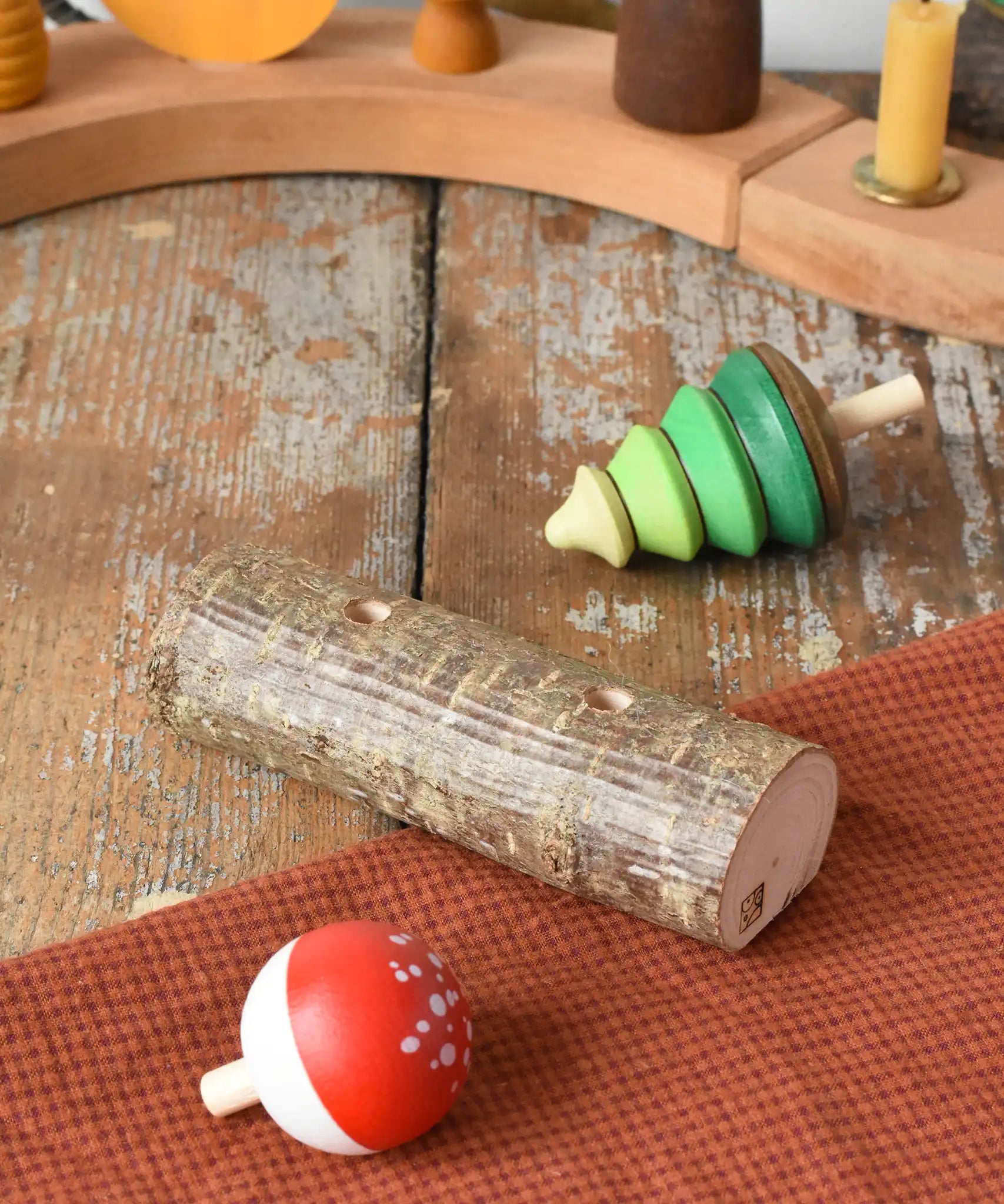 Mader Kreiselmanufaktur forest spinning top set. Green tree spinner and fly agaric mushrrom turn over top that with a branch with two slots. The spinners have been taken out and placed on the wooden desk.