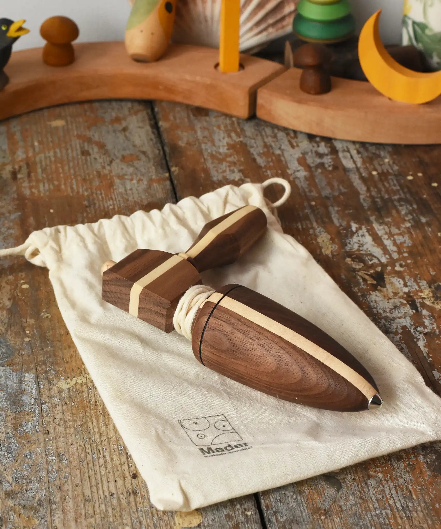 Mader goliath thunderbolt wooden spinning top with starter in a dark wood placed on a cotton drawstring storage bag in the Babipur playroom.