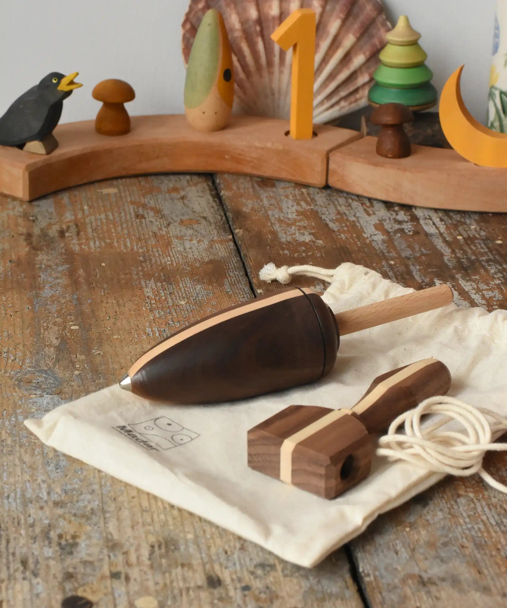Mader goliath thunderbolt wooden spinning top with starter in a dark wood placed on a cotton storage bag in the Babipur playroom.