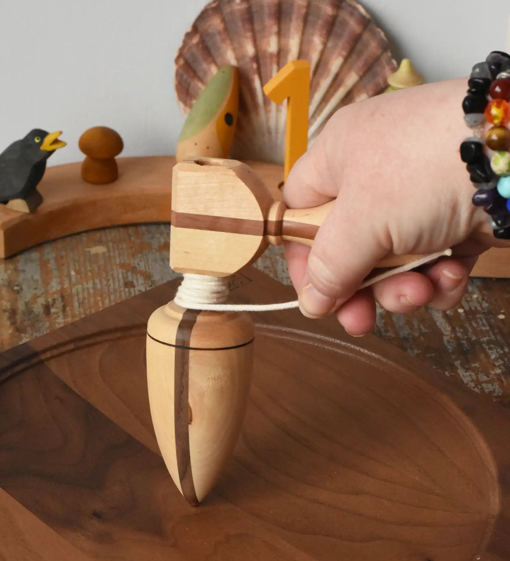 Mader goliath thunderbolt wooden spinning top with starter placed on a walnut spinning plate in the Babipur playroom. It is held upright by and adult's hand.