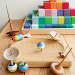 Mader wooden Confetti turn-over spinning top on a Mader spinning plate next to a Grimms Large Stepped Pyramid