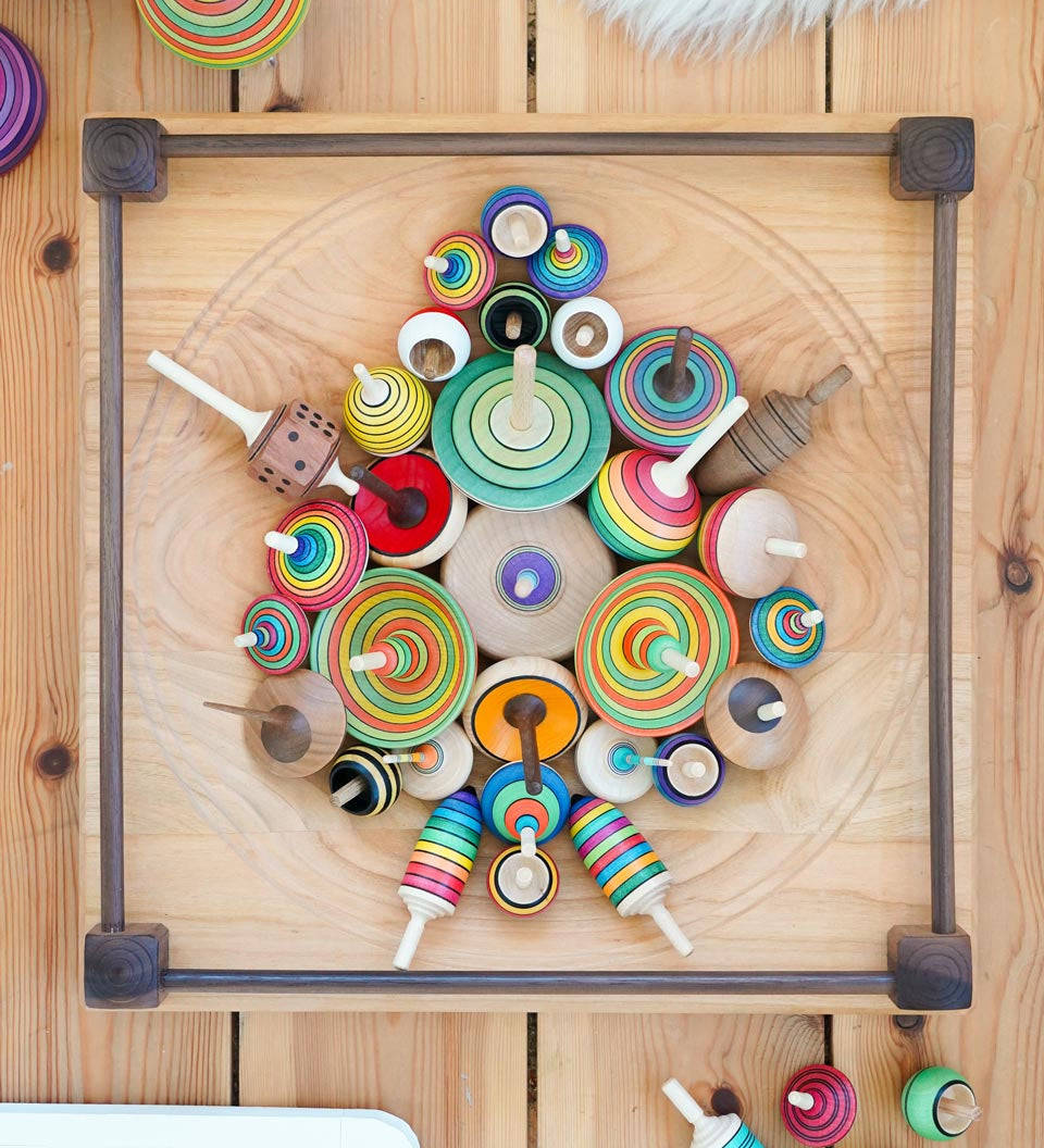 Mader handmade Manege wooden spinning plate on a wooden floor covered in various Mader spinning top toys