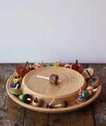 Mader Kreiselmanufaktur 40cm Rondell Ash Wood Spinning Plate placed on a wooden surface in the Babipur playroom. Dice spinning top placed on the top with other spinning tops filling bottom part of the plate. 
