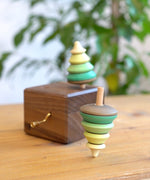 Close up of a Mader spinning top spinning next to a Mader wooden music box