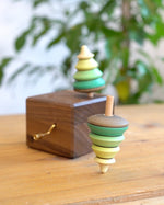 Close up of a Mader spinning top spinning next to a Mader wooden music box