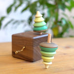 Close up of the Mader spinning tree top spinning next to the Mader wooden music box on a wooden table