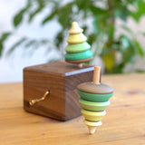 Close up of the Mader spinning tree top spinning next to the Mader wooden music box on a wooden table
