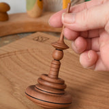 Mader Helene's Captive Rings Apple Spinning Top on an oak spinning plate in the Babipur playroom, am adult hand is holding it upright.