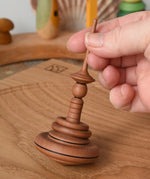 Mader Helene's Captive Rings Apple Spinning Top on an oak spinning plate in the Babipur playroom, am adult hand is holding it upright.