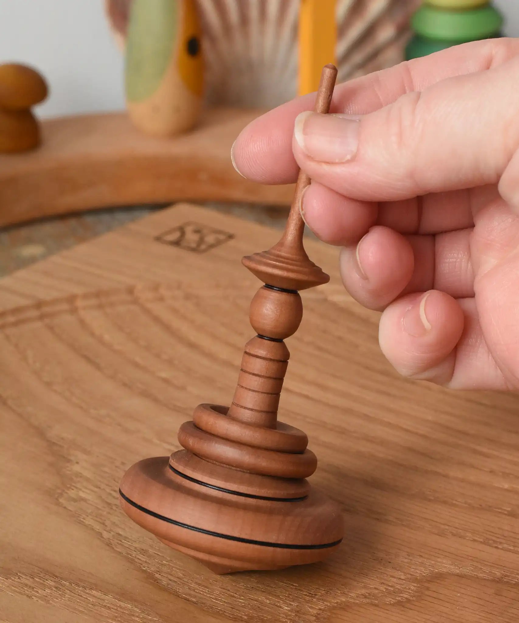 Mader Helene's Captive Rings Apple Spinning Top on an oak spinning plate in the Babipur playroom, am adult hand is holding it upright.