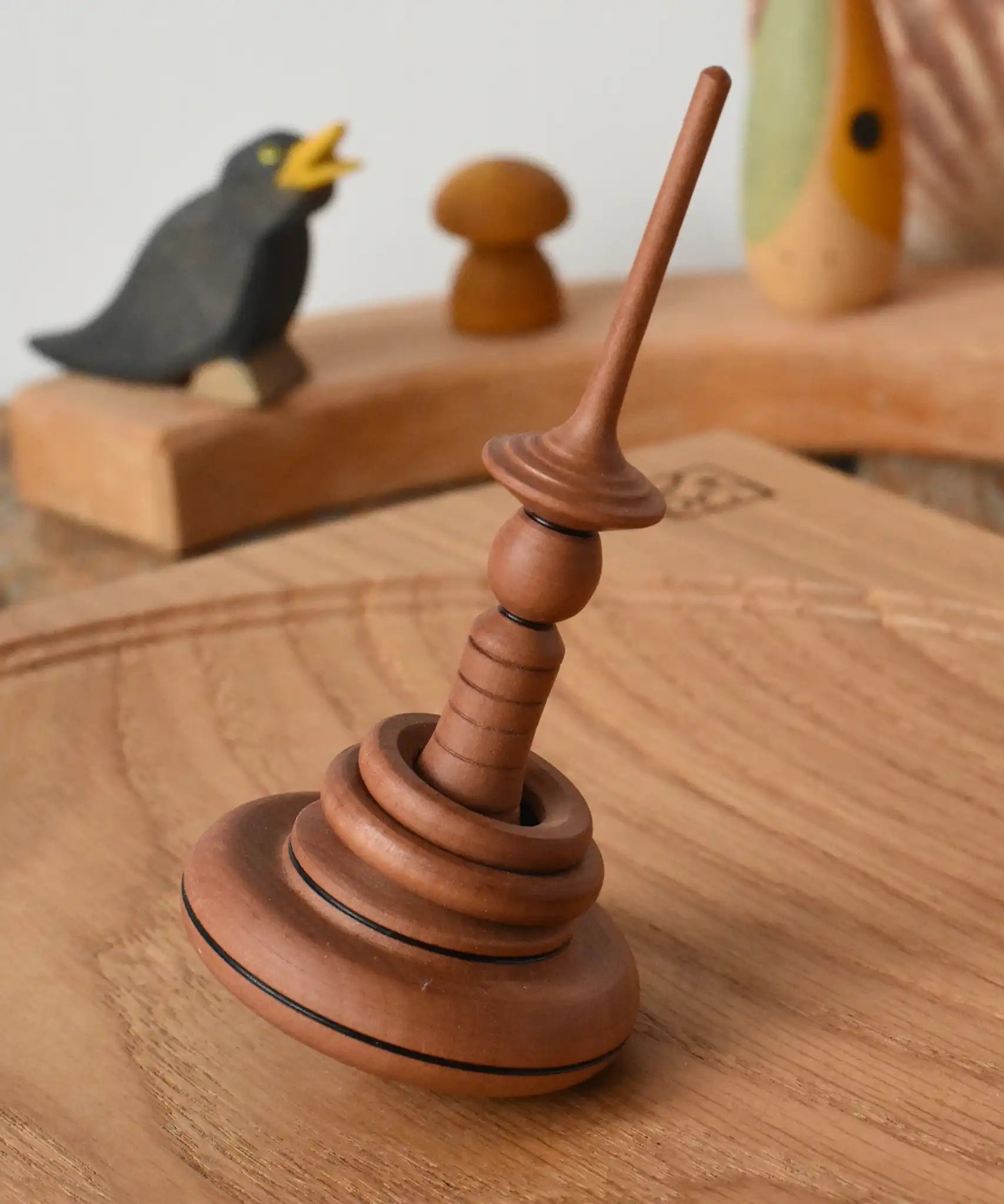 Mader Helene's Captive Rings Apple Spinning Top paced on an oak spinning board.