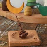Mader Helene's captive rings small plum spinning top with mini board placed on a wooden surface in the Babipur playroom.