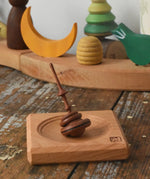 Mader Helene's captive rings small plum spinning top with mini board placed on a wooden surface in the Babipur playroom.