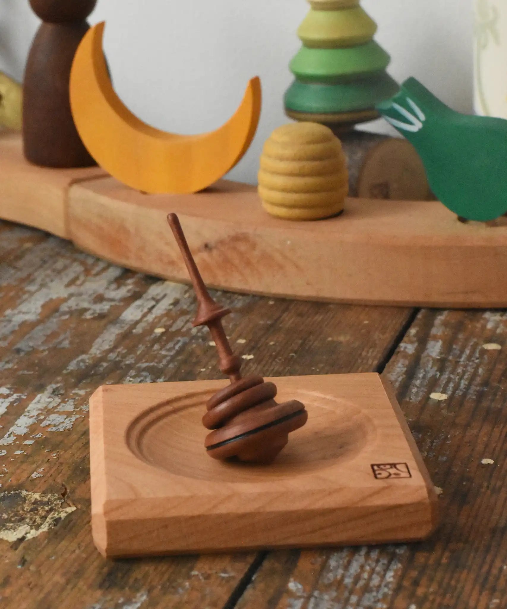 Mader Helene's captive rings small plum spinning top with mini board placed on a wooden surface in the Babipur playroom.