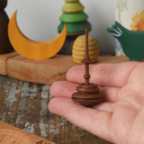 Mader Helene's captive rings small plum spinning top shown in an adult's hand with mini board in the background placed on a wooden surface in the Babipur playroom.