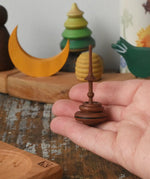 Mader Helene's captive rings small plum spinning top shown in an adult's hand with mini board in the background placed on a wooden surface in the Babipur playroom.