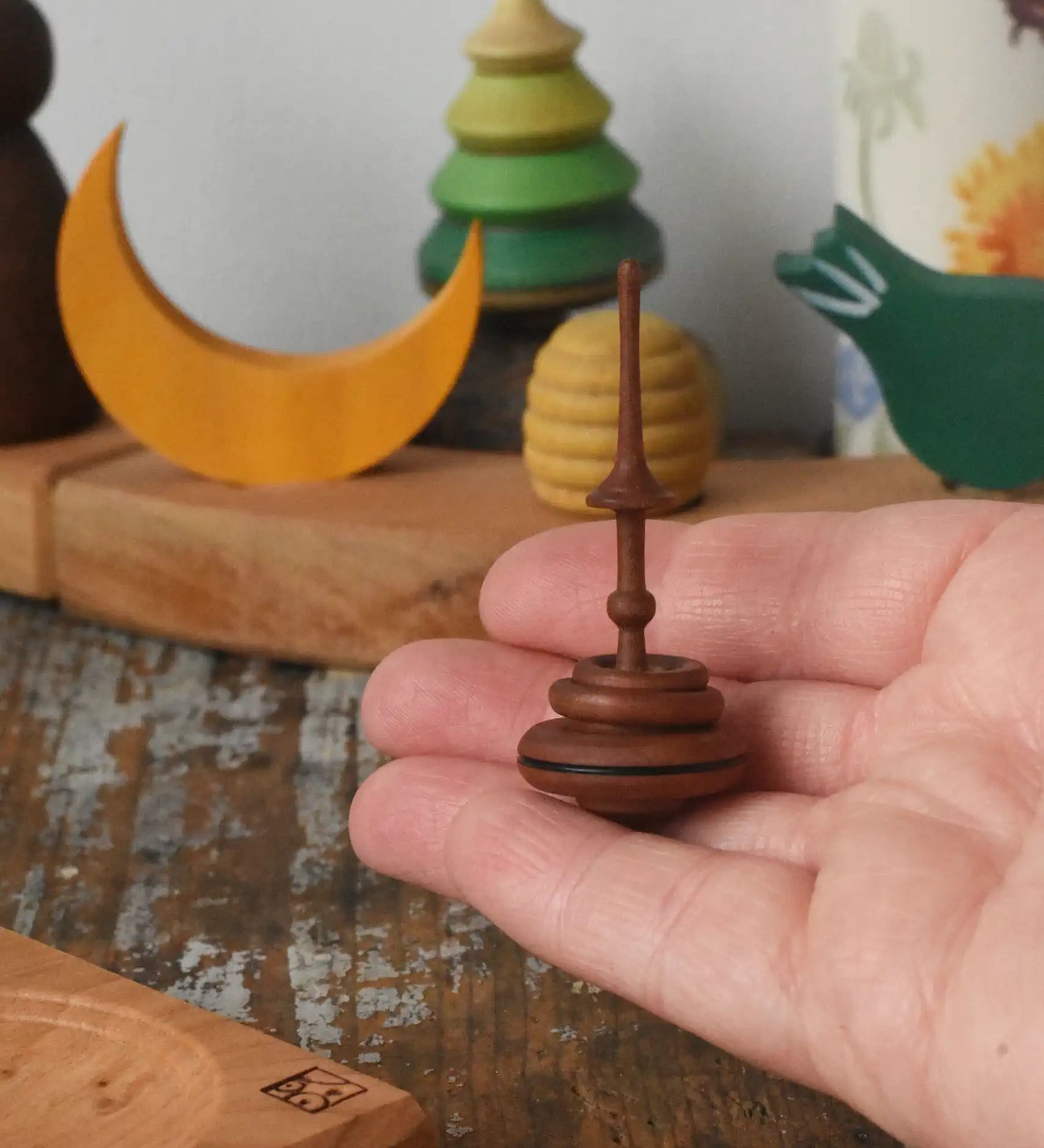 Mader Helene's captive rings small plum spinning top shown in an adult's hand with mini board in the background placed on a wooden surface in the Babipur playroom.