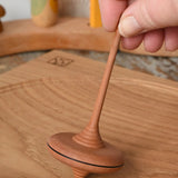 Mader ibis spinning top placed on a wooden desk in the Babipur playroom. The top is held upright by and adult's hand.