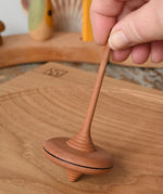 Mader ibis spinning top placed on a wooden desk in the Babipur playroom. The top is held upright by and adult's hand.