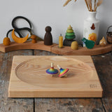 Mader Kreiselmanufaktur Large 25cm ash Spinning Plate with two rainbow spinning tops on it placed on a wooden surface in the Babipur playroom.