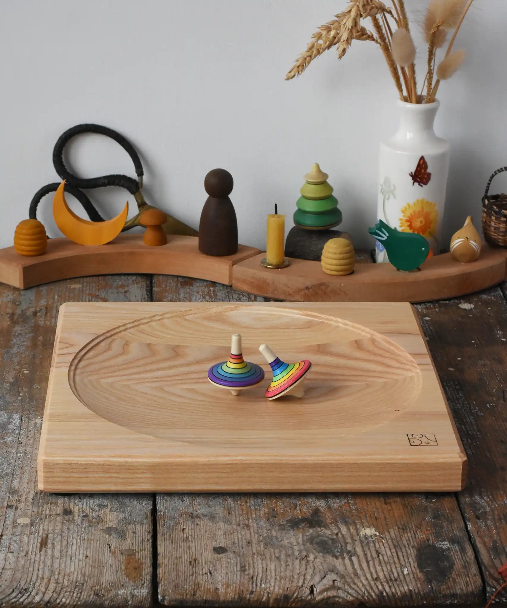 Mader Kreiselmanufaktur Large 25cm ash Spinning Plate with two rainbow spinning tops on it placed on a wooden surface in the Babipur playroom.