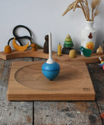 Mader Kreiselmanufaktur 25cm Large Oak Spinning Plate with a blue pull string spinning top spinning on it in the Babipur playroom. 