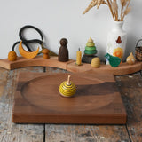 Mader yellow bee spinning top spinning on a Mader Kreiselmanufaktur Large 25cm Walnut Spinning Plate placed on a wooden surface in the Babipur playroom.