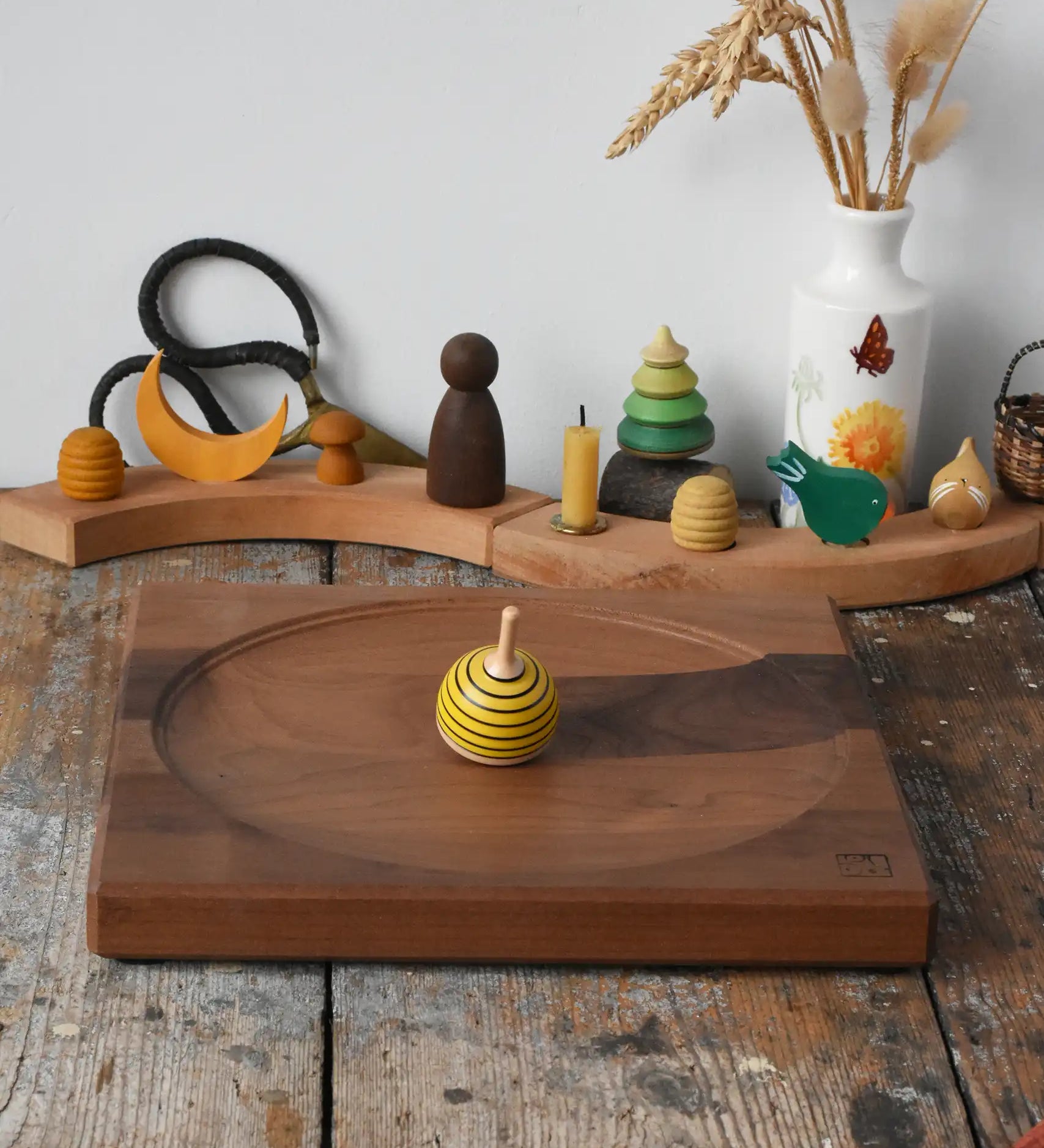 Mader yellow bee spinning top spinning on a Mader Kreiselmanufaktur Large 25cm Walnut Spinning Plate placed on a wooden surface in the Babipur playroom.