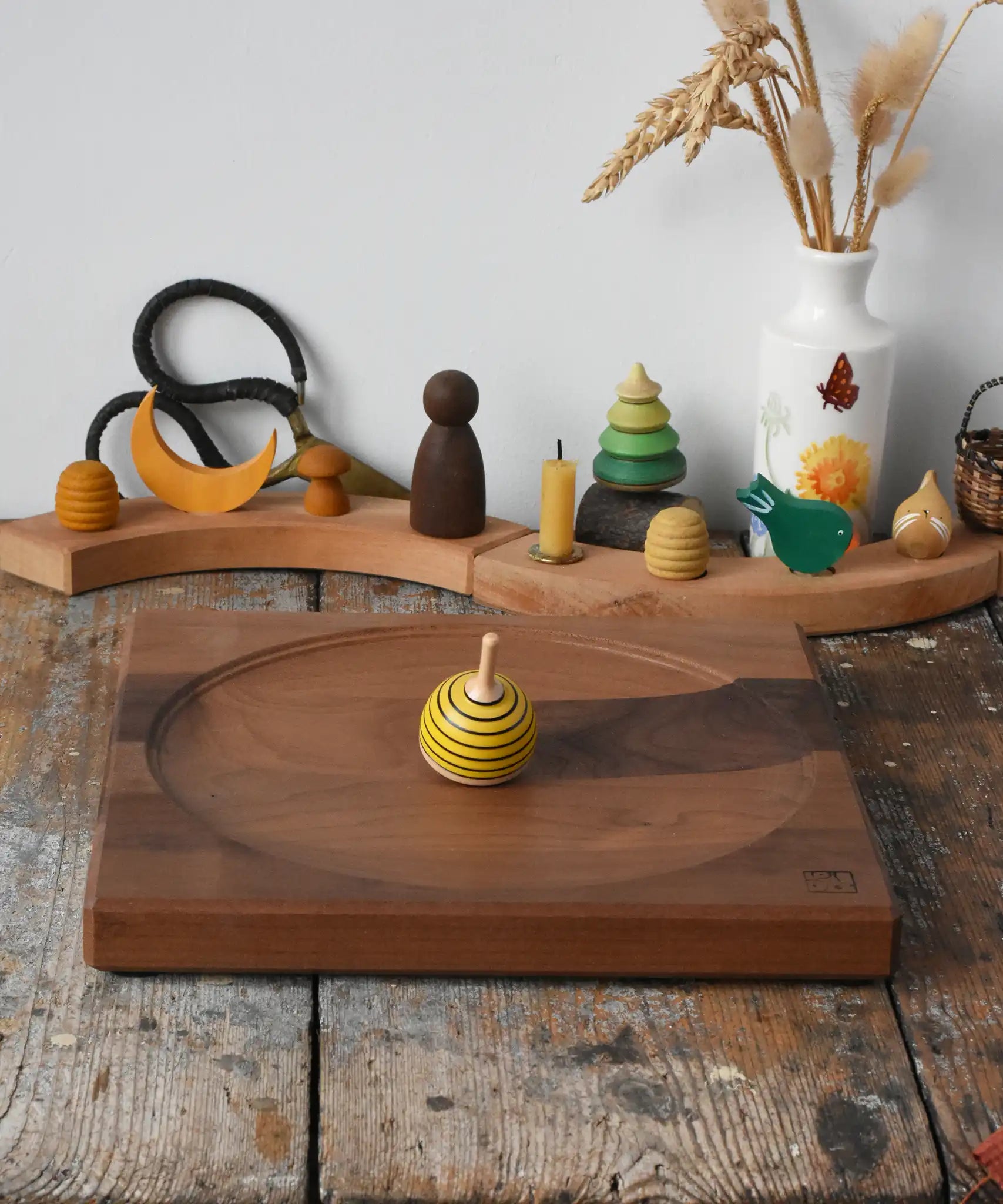 Mader yellow bee spinning top spinning on a Mader Kreiselmanufaktur Large 25cm Walnut Spinning Plate placed on a wooden surface in the Babipur playroom.