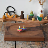 Rainbow spinning tops spinning on a Mader Kreiselmanufaktur Large 25cm Walnut Spinning Plate placed on a wooden surface in the Babipur playroom.