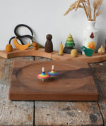 Rainbow spinning tops spinning on a Mader Kreiselmanufaktur Large 25cm Walnut Spinning Plate placed on a wooden surface in the Babipur playroom.