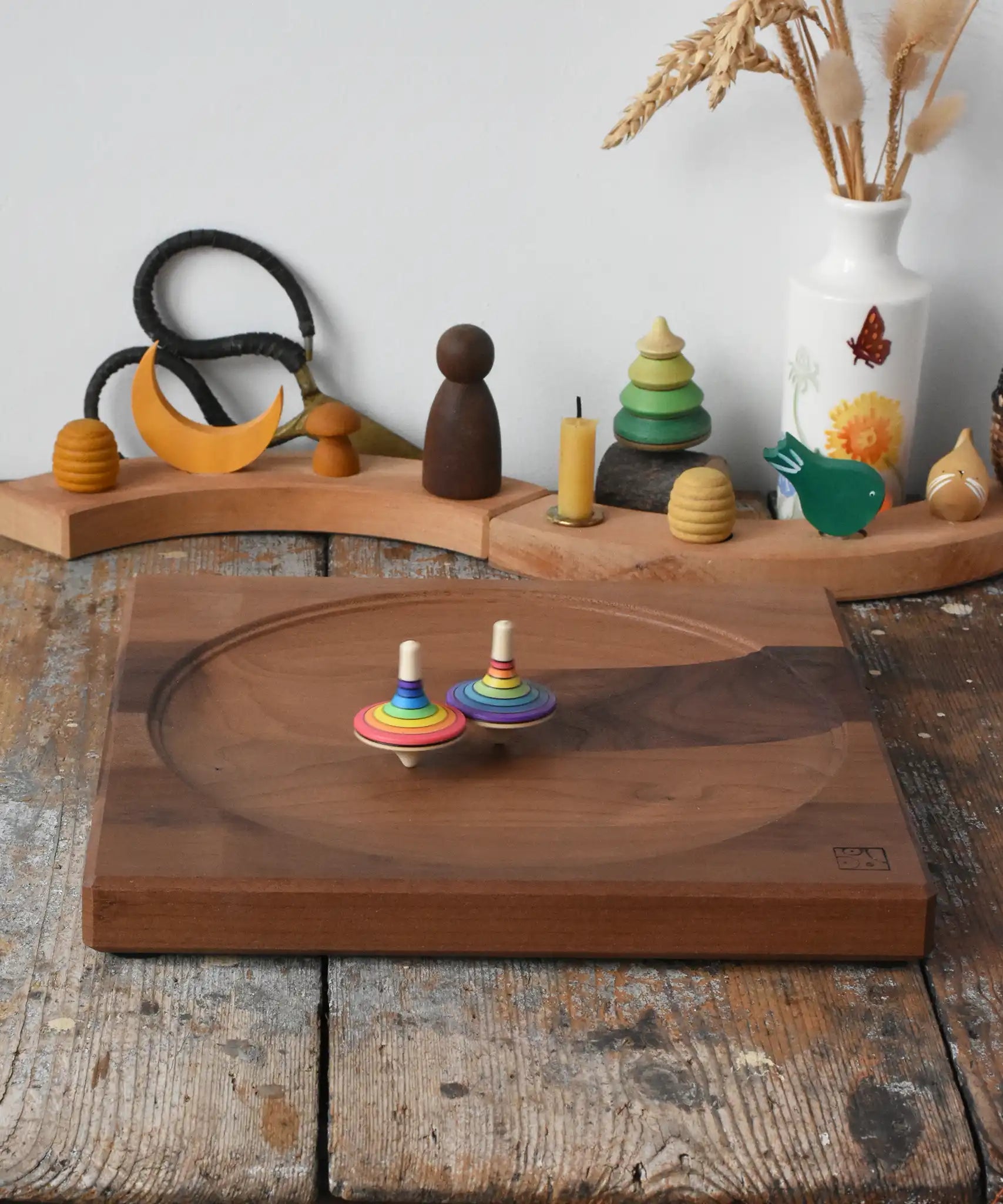 Rainbow spinning tops spinning on a Mader Kreiselmanufaktur Large 25cm Walnut Spinning Plate placed on a wooden surface in the Babipur playroom.