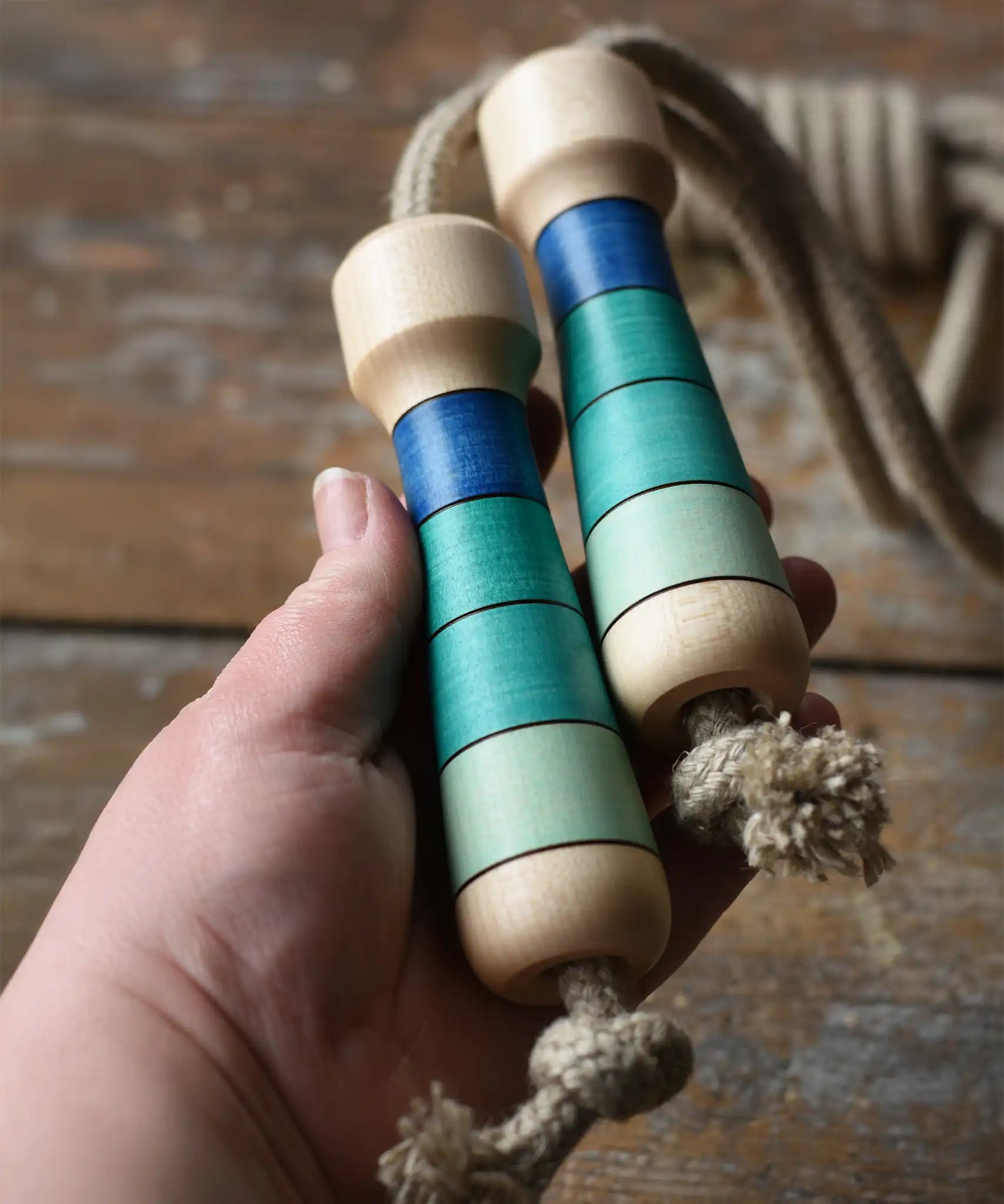 Mader Kreiselmanufaktur Skipping Rope with blue striped wooden handles in an adult's hand. 