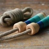 Mader Kreiselmanufaktur Skipping Rope with blue striped wooden handles placed on a wooden surface in the Babipur playroom. 