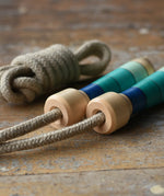 Mader Kreiselmanufaktur Skipping Rope with blue striped wooden handles placed on a wooden surface in the Babipur playroom. 